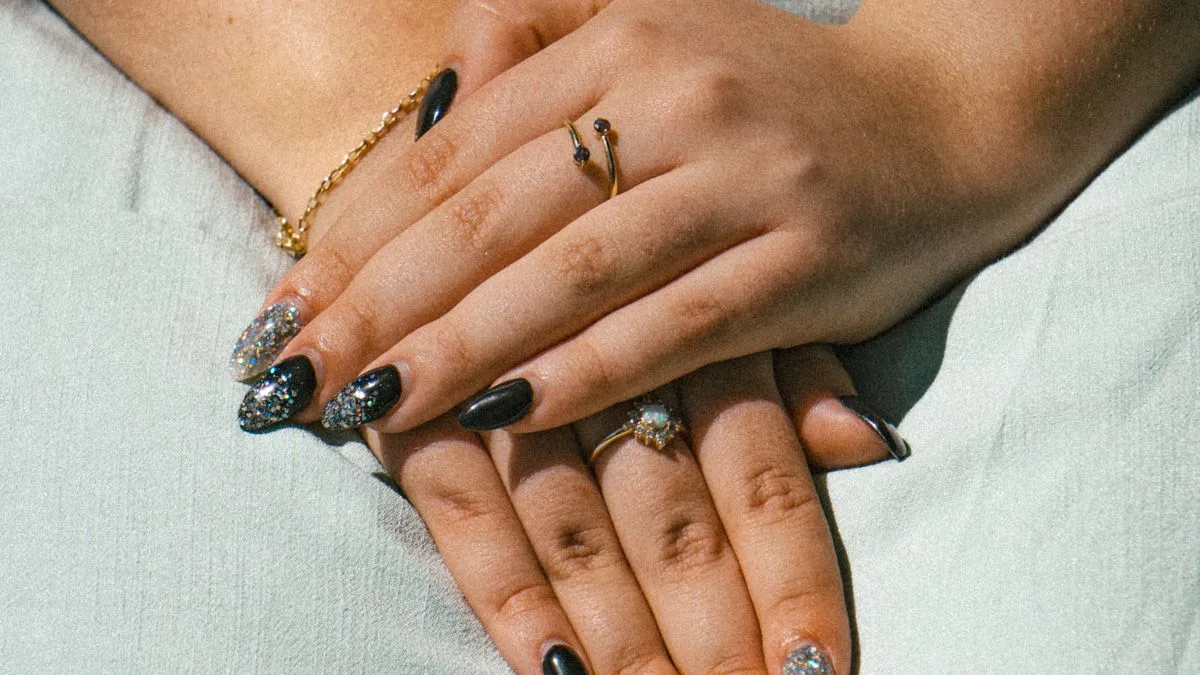 Close-up of glossy black nails layered with silver glitter