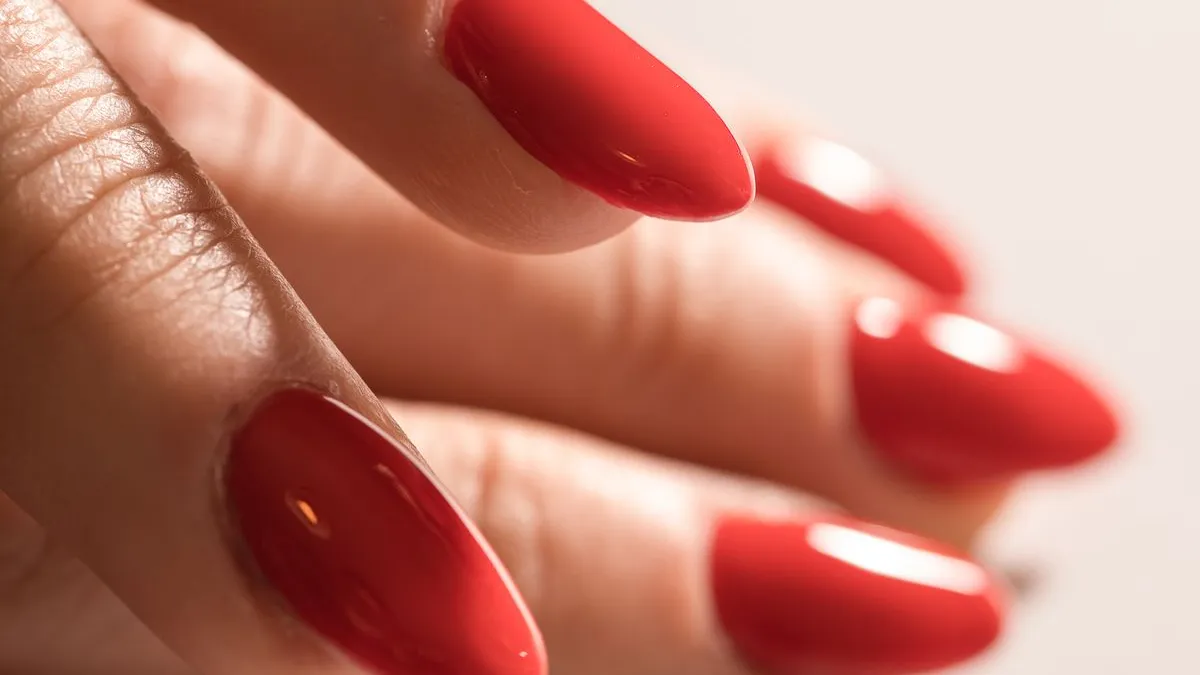 Close-up of glossy bright red almond nails catching the light