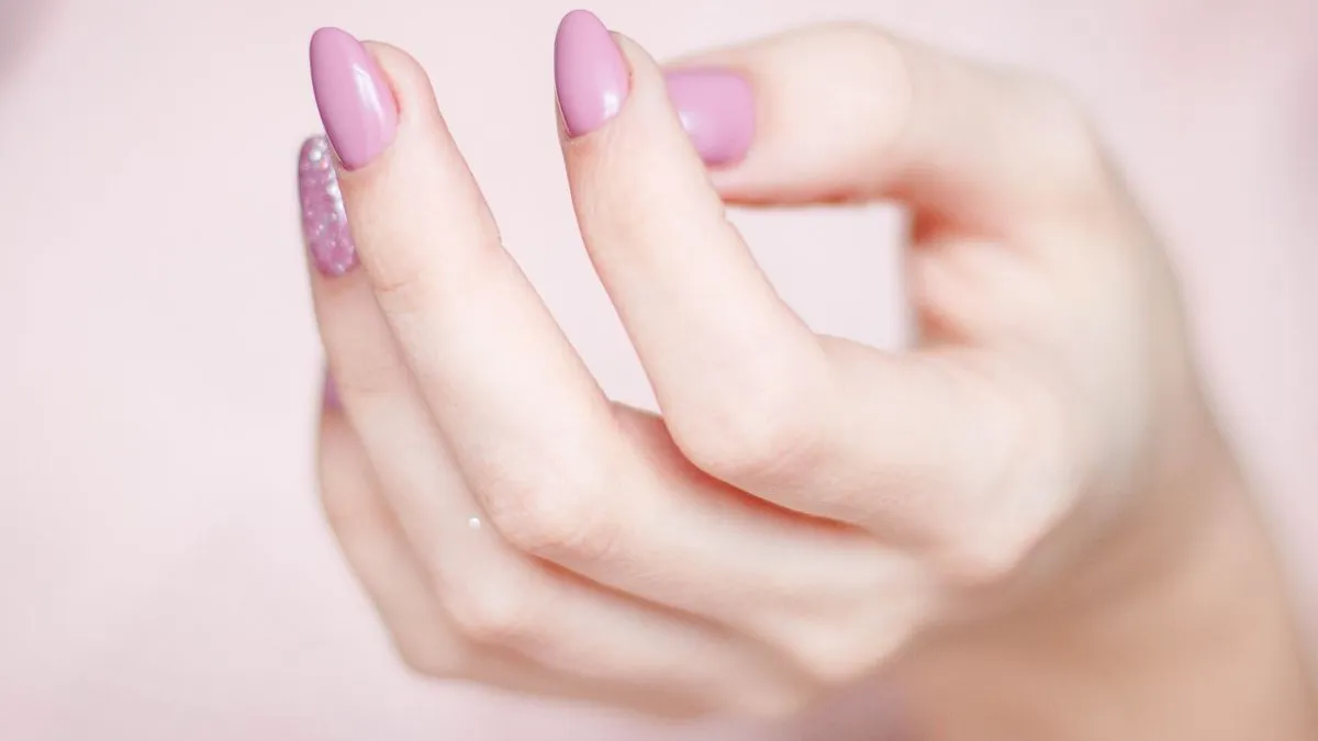 Close-up of a hand with soft lilac almond nails on a pink background